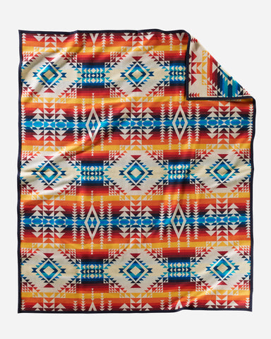 Pendleton wool blanket, with geometric shape patterns in ivory, reds, oranges, and blues, named Pilot Rock.