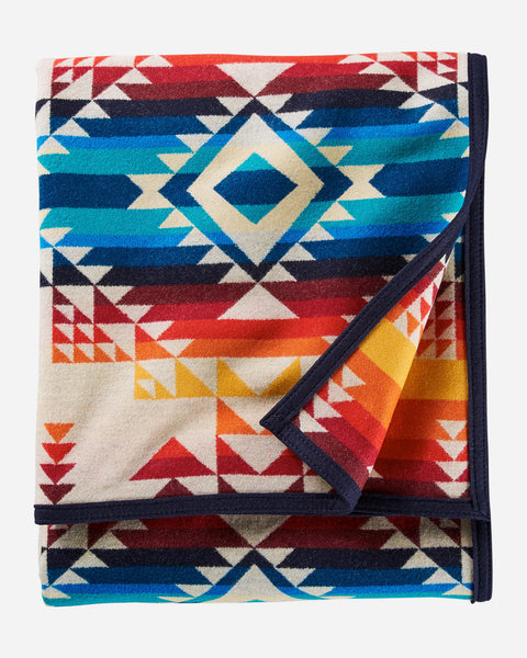 Pendleton wool blanket, with geometric shape patterns in ivory, reds, oranges, and blues, named Pilot Rock.
