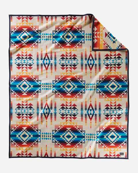 Pendleton wool blanket, with geometric shape patterns in ivory, reds, oranges, and blues, named Pilot Rock.